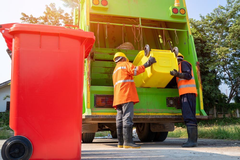 A worker is carefully loading a trash bin into a garbage truck for a junk removal service.